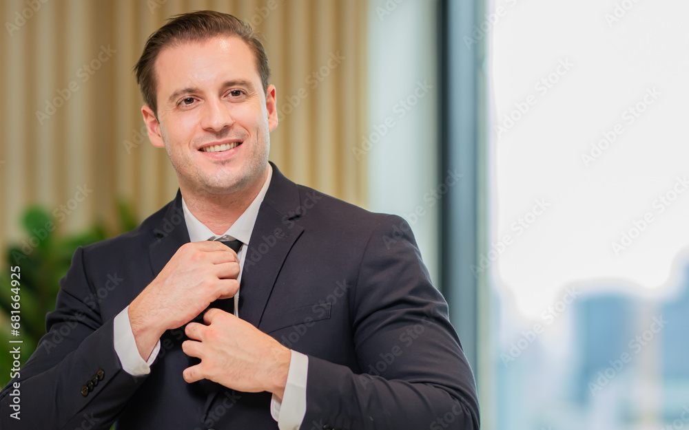 Portrait of handsome Caucasian smart business man wearing formal suit and necktie, smiling with confidence, success and looking at camera with copy space, standing in indoor office. Business Concept.