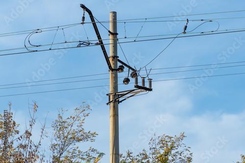 Electrified railway pole on blue sky background. Electric power supply lines on pillars along railway track. Technology of catenary wires. Details structure of voltage system. Equipment of railroad. photo