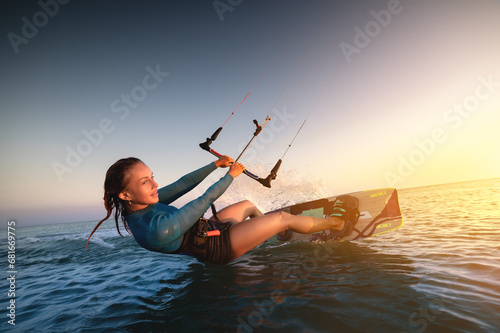 Girl kitesurfing in a sexy hydrosuit with a kite in the sky on board in the blue sea, riding on the water waves. Recreational activities, water sports, activities photo