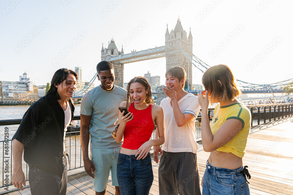 Obraz premium Multiracial group of happy young friends bonding in London city - Multiethnic teens students meeting and having fun in Tower Bridge area, UK - Concepts about youth lifestyle, travel and tourism