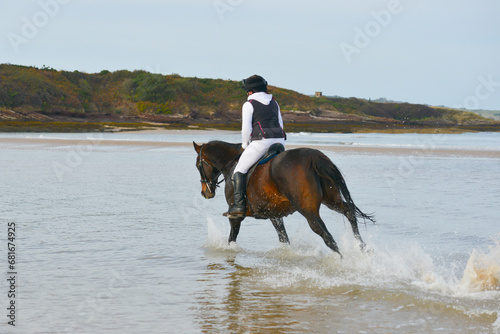 Young woman and her horse pony enjoy riding in the ocean racing along the edge of the sea splashing and having a great time.