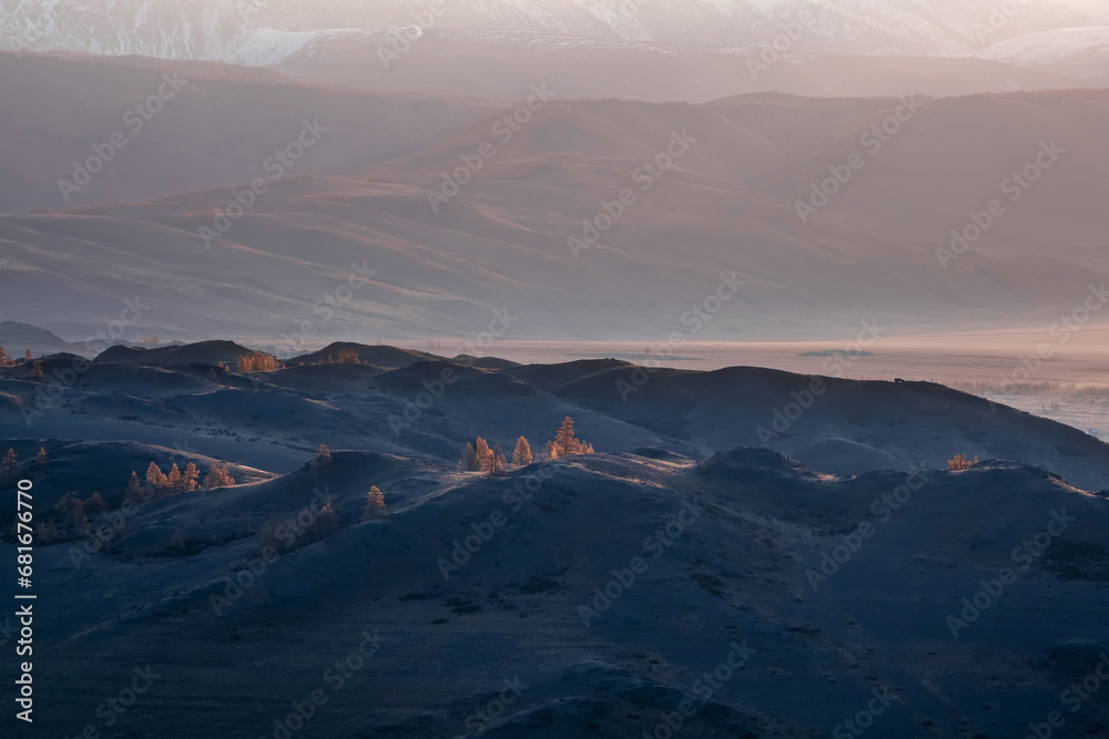 Layers of mountains and autumn trees on distance, soft pink sunset in mountain landscape. Layers of mountains background. Silhouette of the evening mountains at sunset.