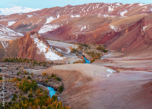 Scenic motley autumn landscape with yellow larch trees on frozen red hills, blue river and mountain range. Vivid autumn colors in mountains. Valley of the Kokorya River in Altai in the early morning. photo