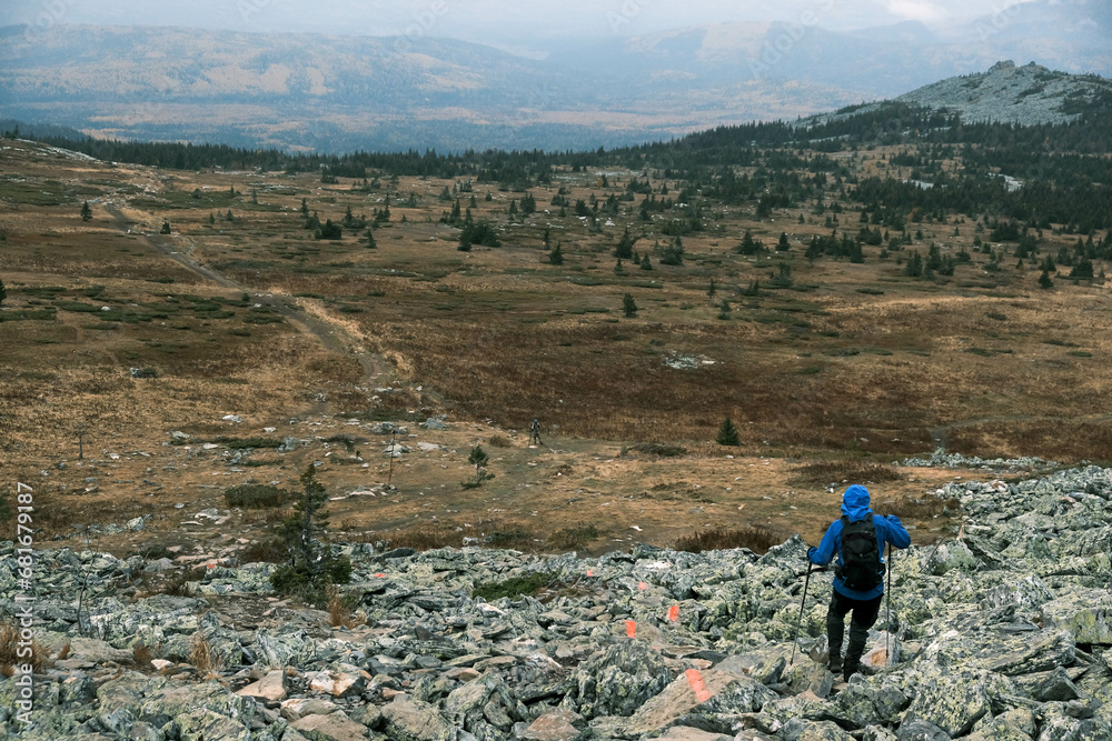 Obraz premium a male tourist descends from the mountain with trekking poles,ahead of a mountain landscape with fog 