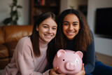 Two teenager girl friends in a house holding a piggybank