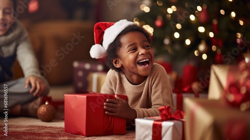 little boy opening pile of presents and smiling with excitement while his fam...