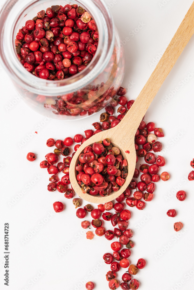 Aromatic spice pink pepper seeds in wooden spoon and glass jar top view on white background