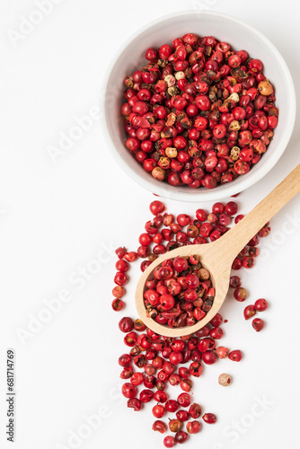 Fragrant spice pink pepper seeds in wooden spoon and a  white ceramic bowl top view. Close up pink peppercorn isolated