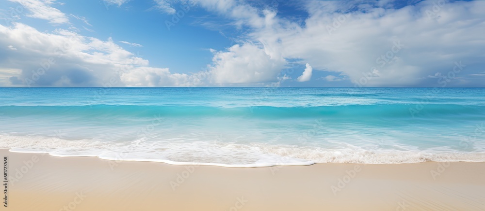 As the gentle waves crash onto the golden sand of the beach, the sun bathes the landscape in a warm, golden light, reflecting off the crystal clear blue water of the ocean; the texture of the sand