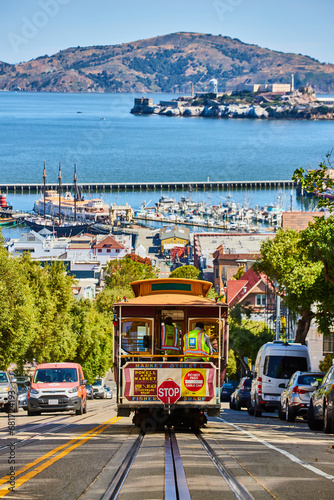Trolley streetcar going down steep, sunny road with Alcatraz Island in San Francisco Bay, CA photo