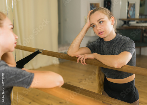 Female ballet dancer resting at barre and mirror in dance studio - dance and ballerina concept