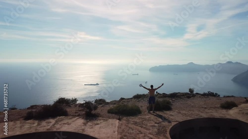 Young boy running over military ruins on top of a mountain. He runs up to the peak and raises his arms, looking at the sea and the mountains. Feeling of freedom and self-improvement. Monte Roldan 