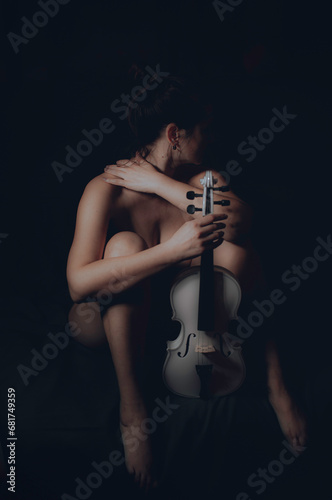 Nude girl with a beautiful body in the twilight with a white violin