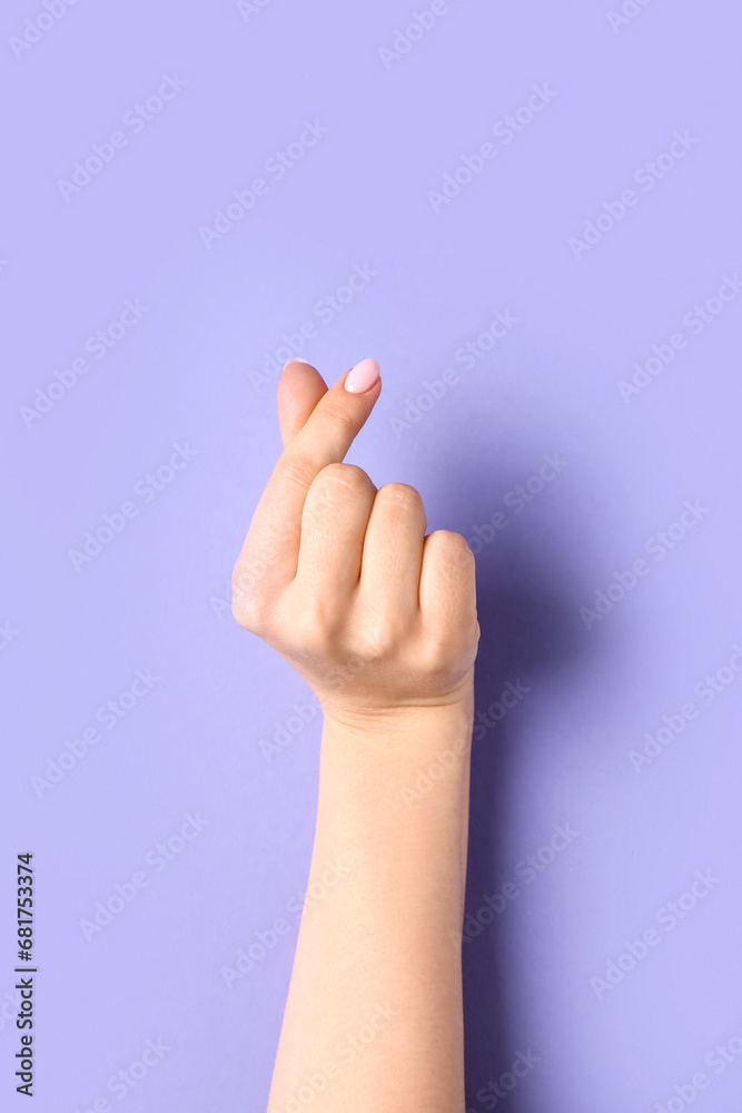Woman making heart with her fingers on lilac background