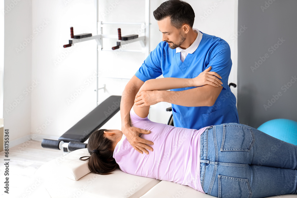 Male physiotherapist working with young woman on couch in rehabilitation center - obrazy, fototapety, plakaty 