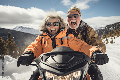 Pareja senior de hombre y mujer de la tercera edad, divirtiendose montados en una moto de nieve bajando por una montaña nevada en invierno photo
