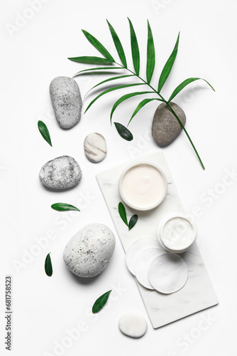 Composition with cosmetic products, spa stones and palm leaf on white background