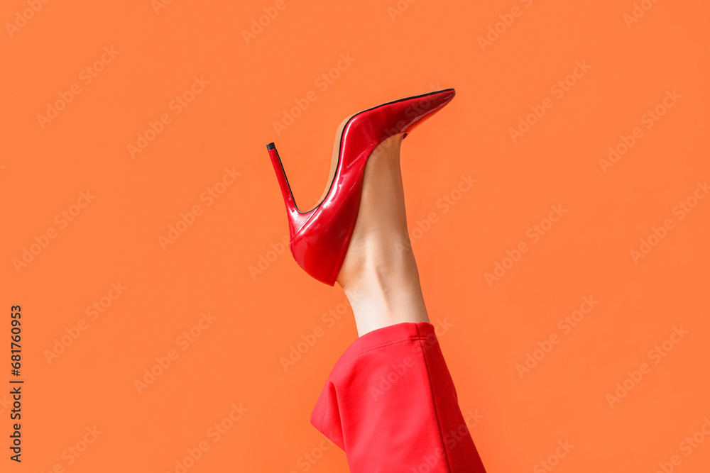 Leg of young woman in stylish red high heel on orange background - obrazy, fototapety, plakaty 