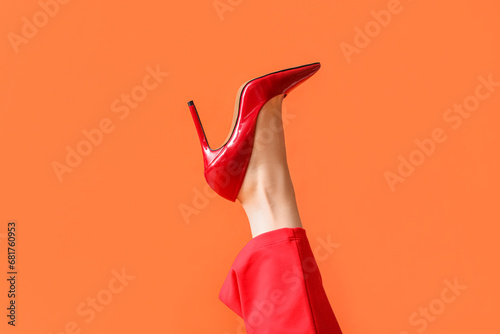 Leg of young woman in stylish red high heel on orange background
