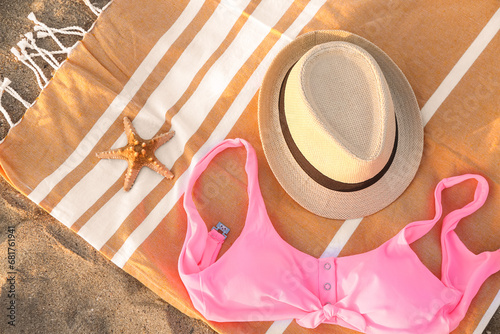 Towel with stylish straw hat and bikini bra on sand