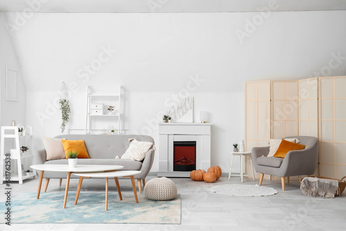 Interior of light living room with electric fireplace  pumpkins and sofa