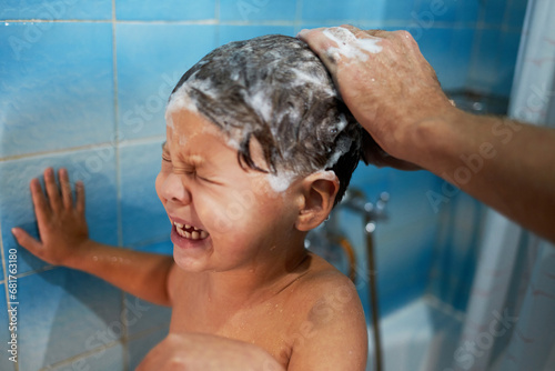 Dad's hands wash the little boy's head in the bathroom. The child does not like to wash his hair and cries.