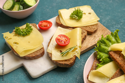 Tasty sandwiches with cheese and tomatoes in board on green background, closeup