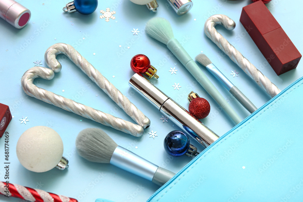 Cosmetic bag with different makeup products and Christmas decor on blue background, closeup Cosmetic bag with different makeup products and Christmas decor on blue background, closeup