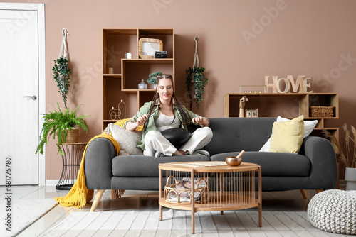 Young woman with sticks playing glucophone on sofa at home