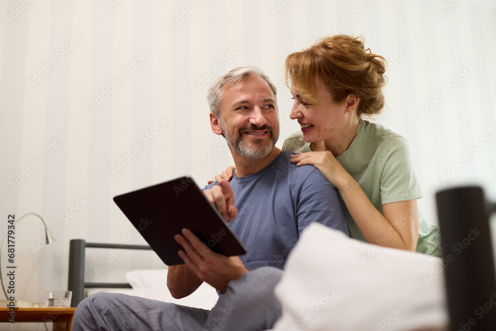 Smiling mature couple using digital tablet at home in bed