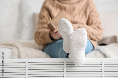 Young woman warming legs on radiator in bedroom, closeup