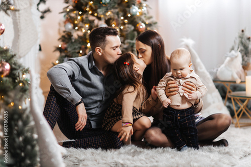 Happy family having fun together against the background of a New Year tree and Christmas decor. Young dad and happy mother with son and daughter smile and enjoy New Year holidays