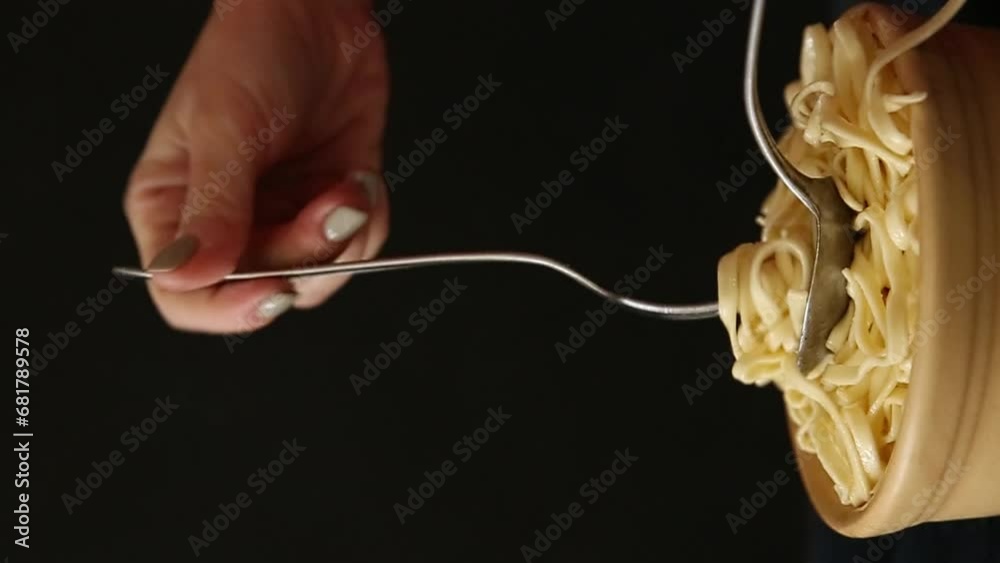 A white woman rolling cooked spaghetti with a fork and spoon