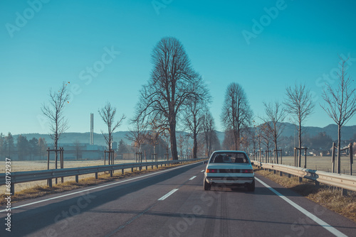 Old vintage european car from the seventies is driving through early morning cold countryside. Rear view, close to Logatec and its avenue. photo