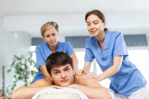 Two women doing back massage to man lying on massage table in a spa salon © JackF