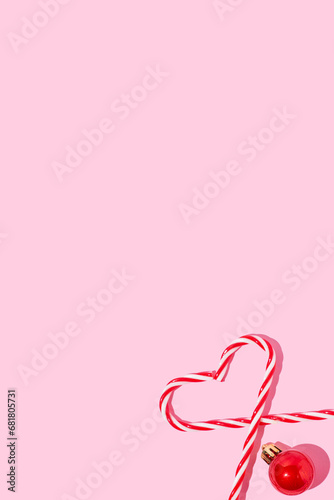 Heart shape made of candy cane and red Christmas ball  on pink background.. Christmas pattern. Minimal holiday concept. Copy space.
