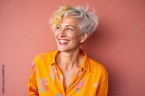 Portrait of a happy senior woman laughing against a pink background.