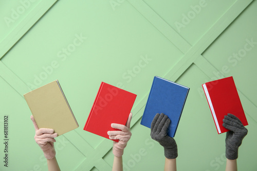 Female hands in warm gloves with different books against color wall