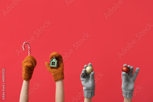 Female hands in warm gloves with Christmas decorations on red background