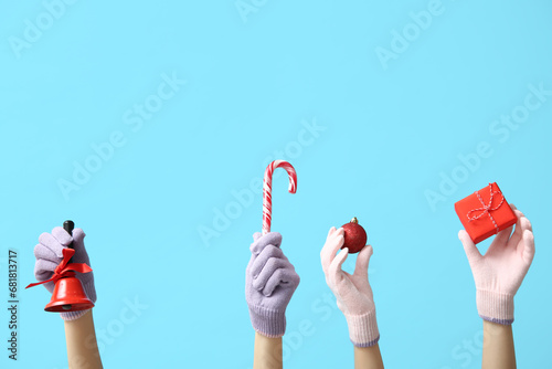 Female hands in warm gloves with Christmas decorations on color background