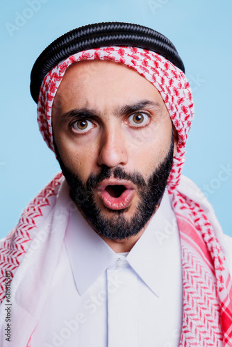 Muslim man with open mouth wearing traditional checkered ghutra headscarf studio closeup portrait. Arab person in islamic headdress showing emotion on face and looking at camera