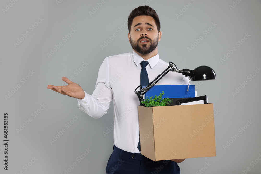 Confused unemployed man with box of personal office belongings on light grey background Confused unemployed man with box of personal office belongings on light grey background