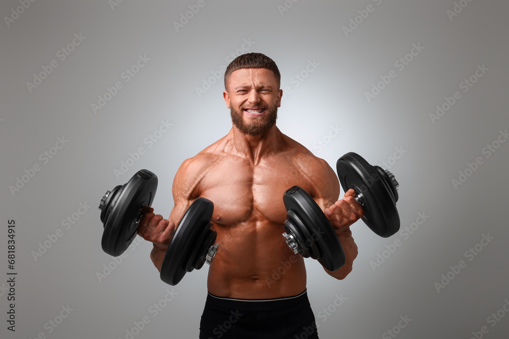 Emotional young bodybuilder exercising with dumbbells on light grey background Emotional young bodybuilder exercising with dumbbells on light grey background
