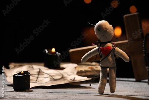 Voodoo doll pierced with pins and ceremonial items on wooden table against blurred background photo