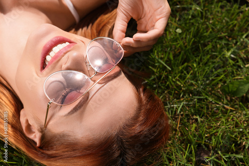 Beautiful woman in sunglasses on green grass outdoors, space for text