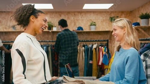 Female customer buying shirt from sales assistant at cash desk  and making contactless payment with credit or debit card in fashion or clothes store with customers in background - shot in slow motion photo