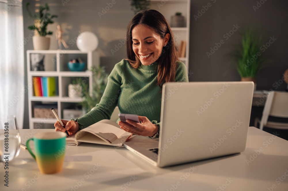 A woman is using cellphone while writing in textbook at home office. A woman is using cellphone while writing in textbook at home office.