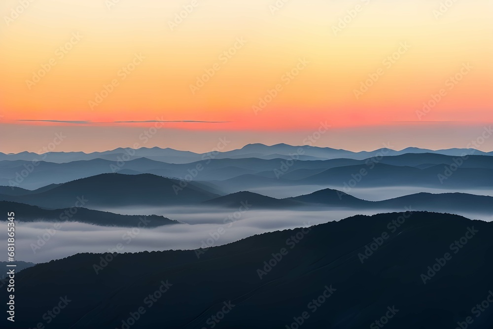 霧に覆われた山脈：オレンジと黄色のグラデーションが広がる空と、地平線上の薄いピンクの線、そして青と灰色の山々が霧やもやに覆われている、日の出または日没の風景