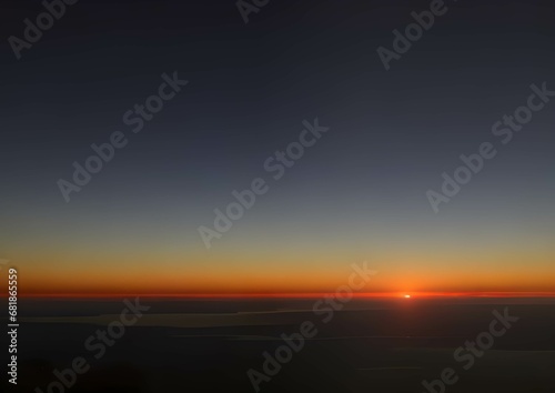 夜明けの地平線に昇るオレンジ色の太陽と青い空のグラデーション