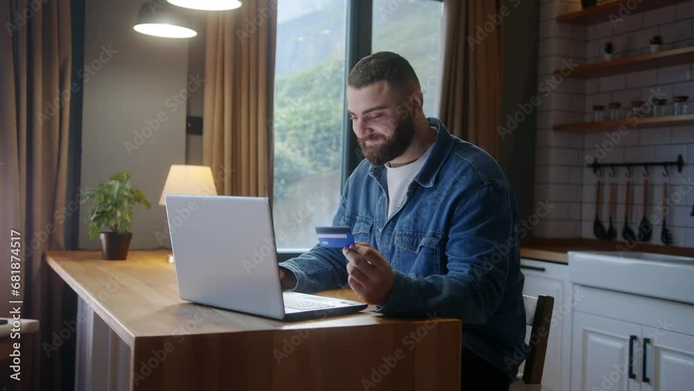 Smiling young adult man sitting against the kitchen counter entering credit card number on laptop for makes secure easy distant electronic payment at home
Smiling young adult man sitting against the kitchen counter entering credit card number on laptop for makes secure easy distant electronic payment at home